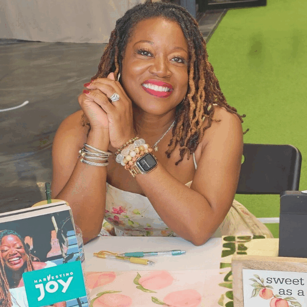 Author Andrea Harvey sitting at a peach-themed table during her Harvesting Joy book signing, surrounded by garden-inspired decor and smiling warmly.